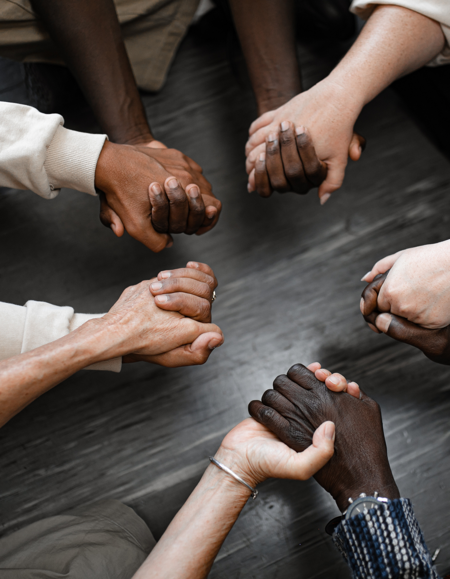 Hands of people from different racial backgrounds held together in a circle on a wooden floor.