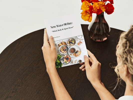 Woman holding the New Wave 90 Day: Mind, Body & Spirit Reset Transformation digital wellness program booklet on a dark wooden table. Ideal for Christian health and fitness journeys.